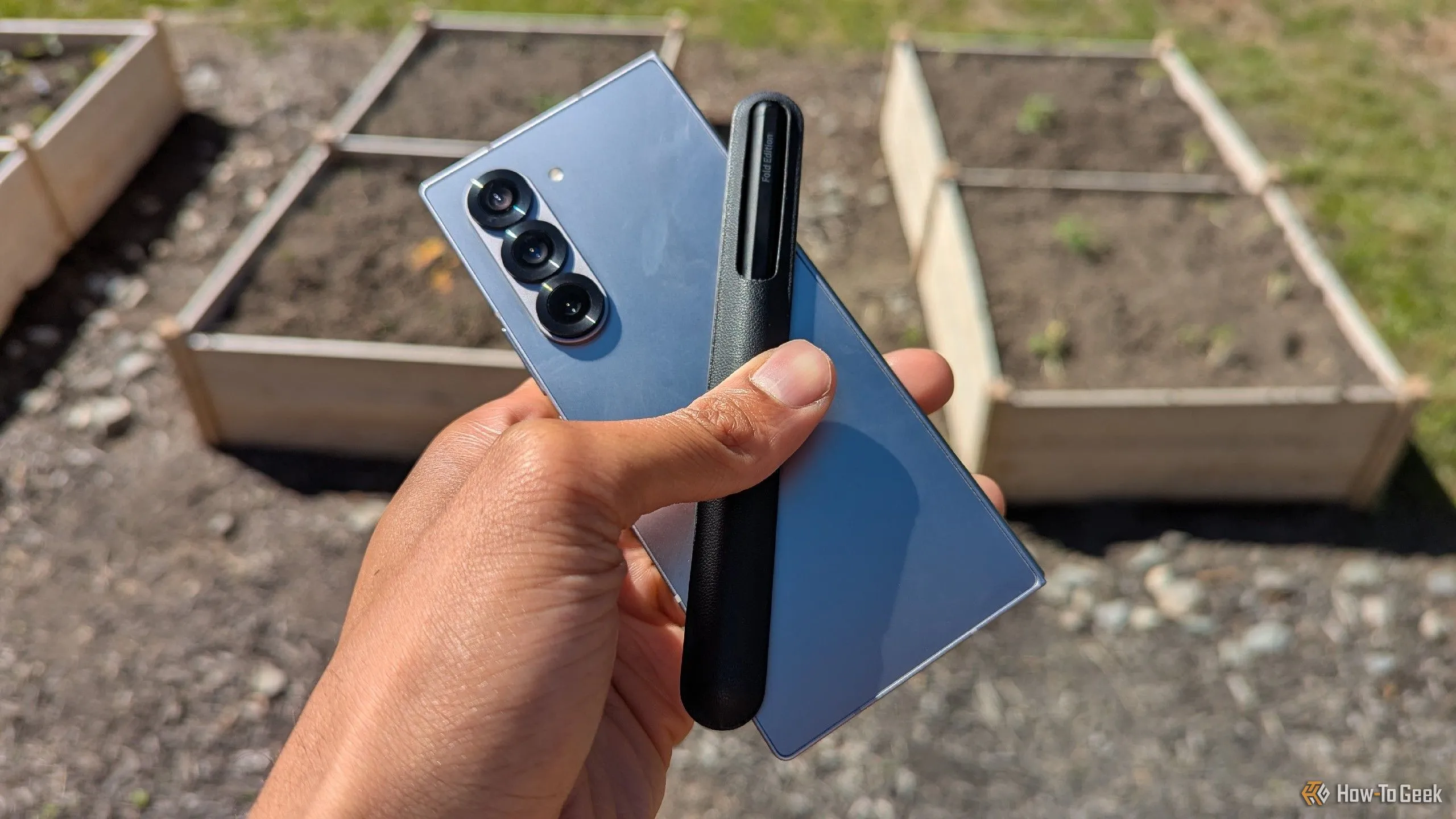 Điện thoại Galaxy Z Fold 6 màu xanh navy kèm bút S Pen nổi bật trước khung cảnh vườn cây xanh tươi.