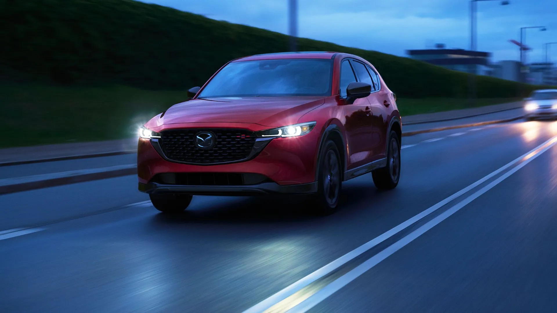Hình ảnh Mazda CX-5 2025 màu đỏ di chuyển trong đô thị buổi tối, minh họa thiết kế ngoại thất.