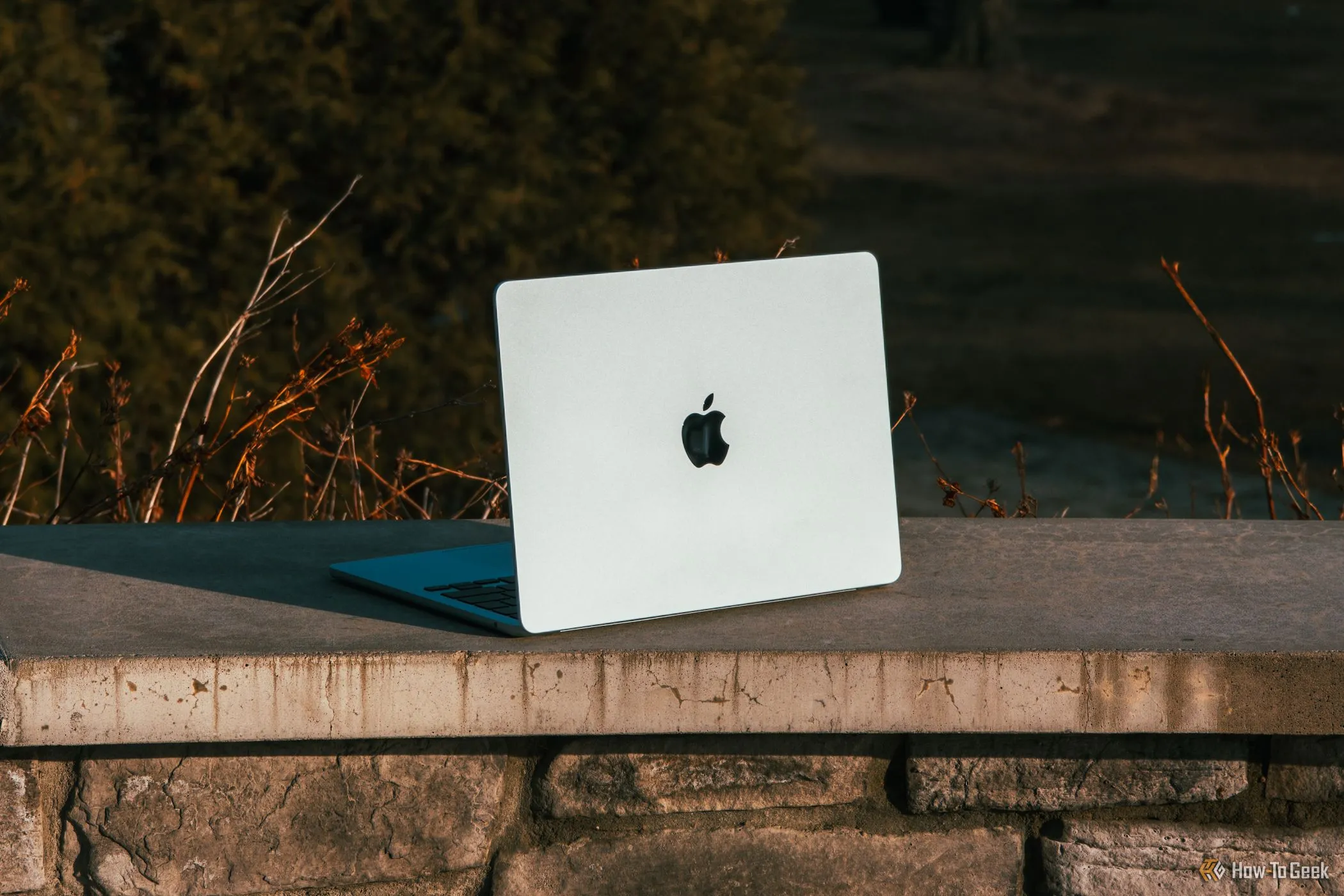 Laptop MacBook Air M4 màu xanh lam đặt nghiêng trên gờ bê tông dưới ánh nắng