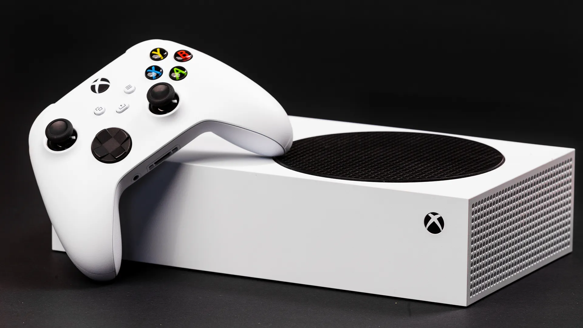 Máy chơi game Xbox Series S màu trắng và tay cầm điều khiển trên bề mặt phẳng.