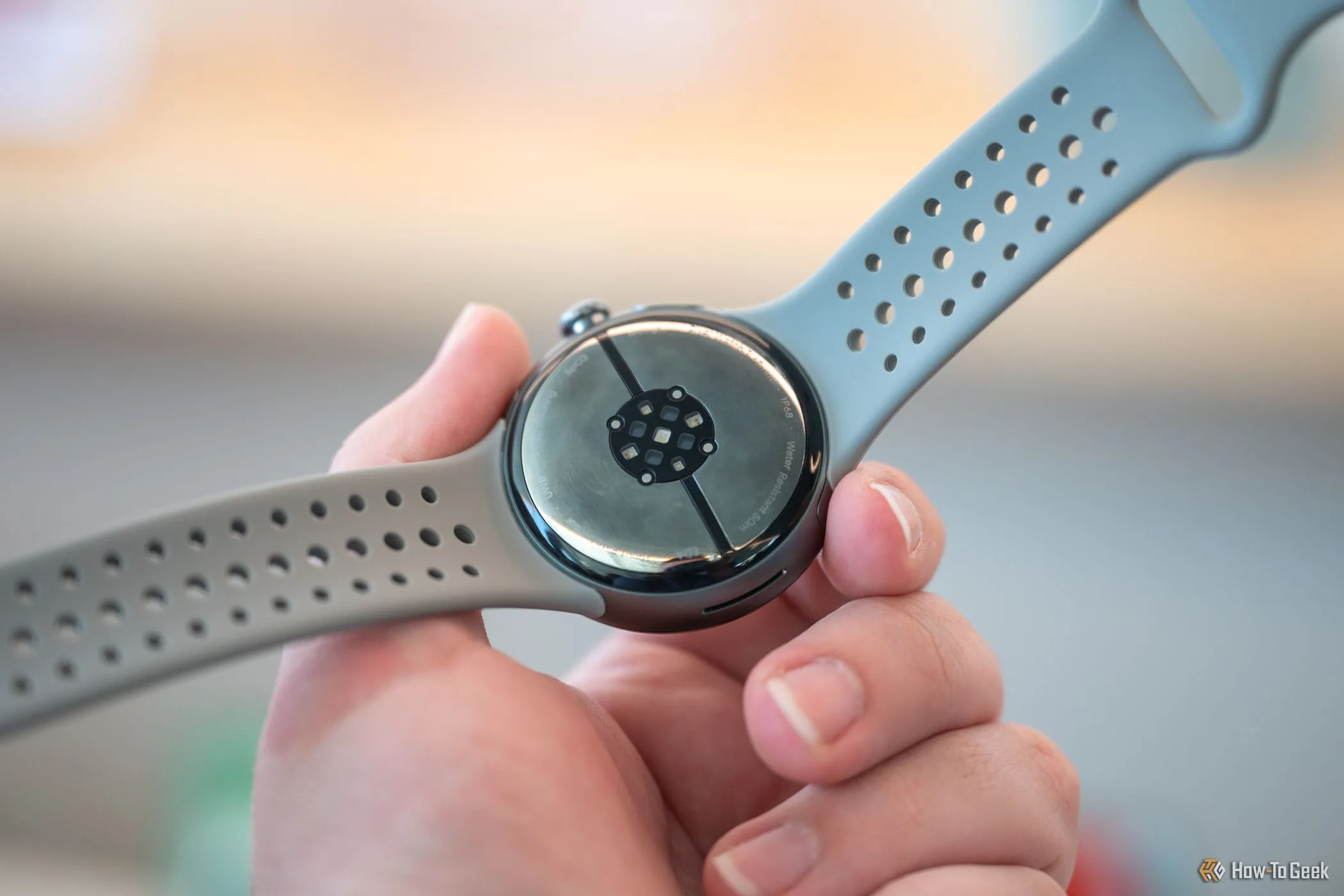 Người dùng cầm Google Pixel Watch 3, hiển thị các cảm biến mặt dưới và khu vực kết nối dây đeo độc quyền