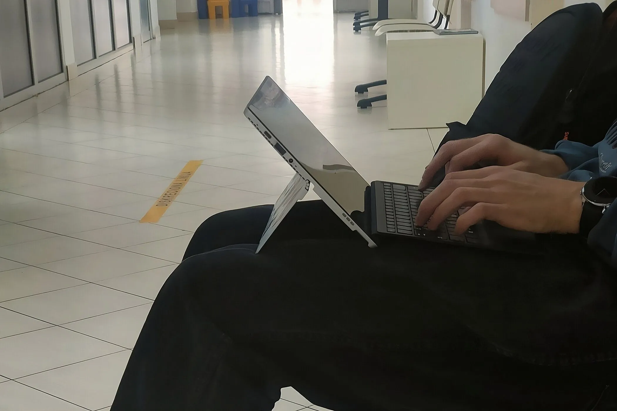 Người dùng đang gõ phím trên một chiếc laptop 2 trong 1 đặt trên đùi, minh họa cách sử dụng thiết bị di động thoải mái.