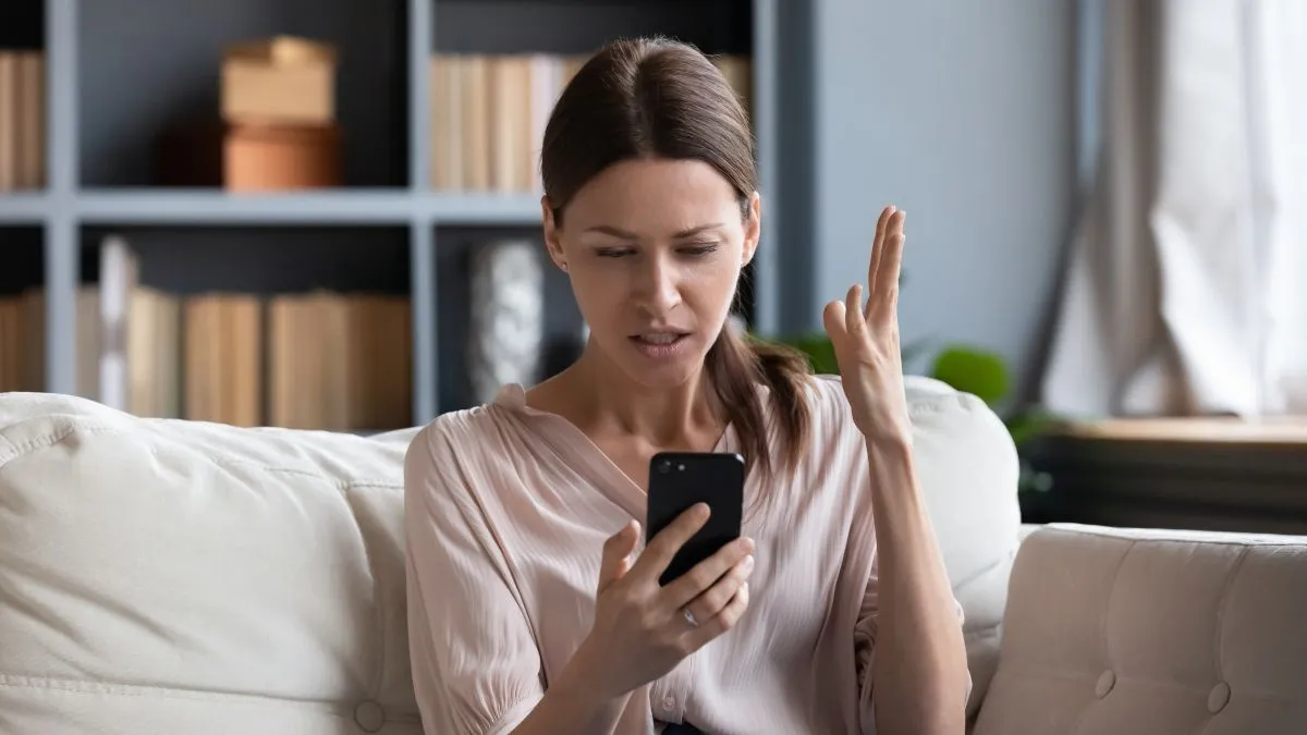 Người phụ nữ biểu cảm khó chịu khi dùng điện thoại, tượng trưng cho trải nghiệm đọc có bình luận tiêu cực.