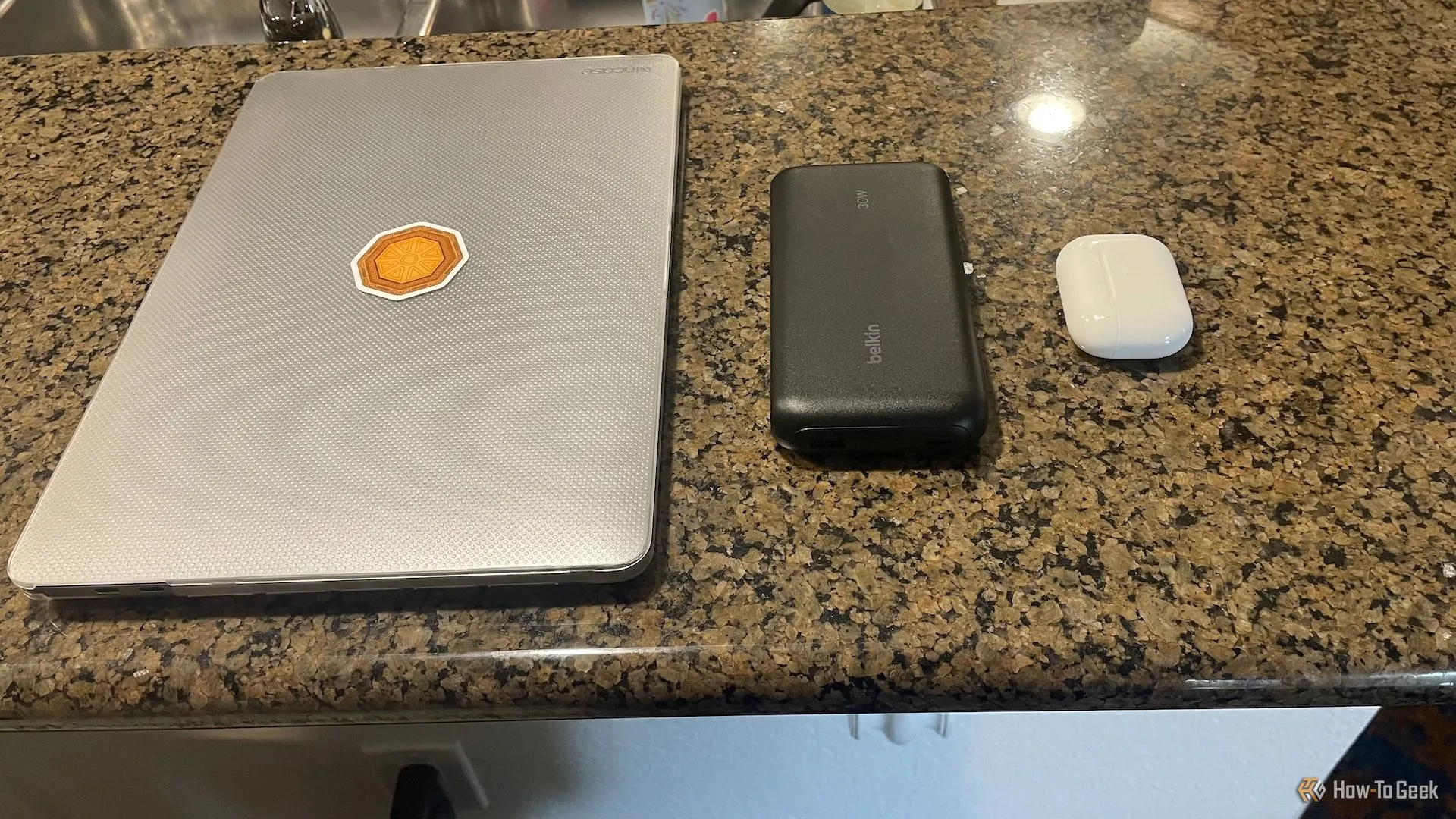 So sánh kích thước Belkin BoostCharge 20K bên cạnh MacBook Pro và hộp sạc AirPods, cho thấy tính di động.