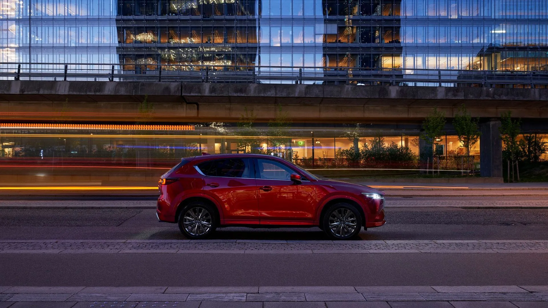 Thiết kế thân xe Mazda CX-5 2025 màu đỏ khi xe di chuyển trên đường phố về đêm.