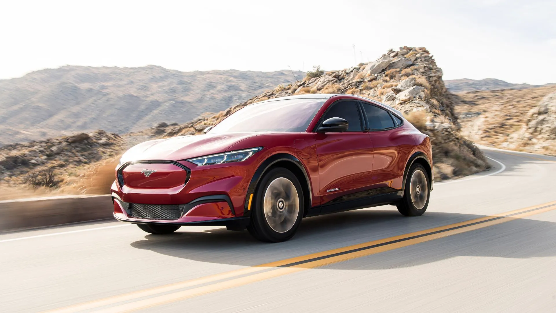Xe điện Ford Mustang Mach-E màu đỏ đời 2021 đang di chuyển trên đường nông thôn với núi non phía sau, minh họa lỗi khóa cửa và hệ thống điện.